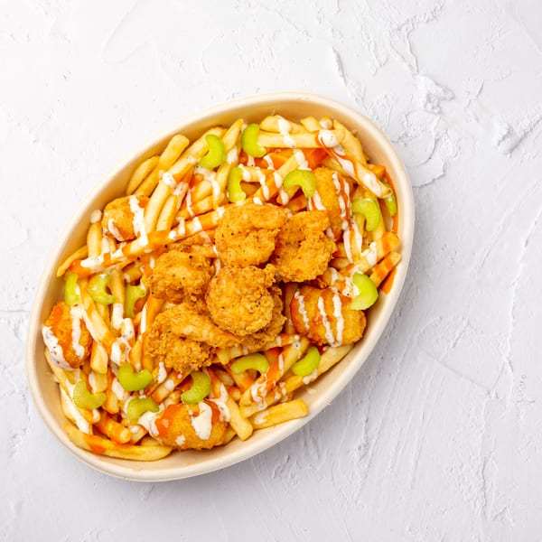 Crispy fried chicken pieces atop French fries with celery, carrots, and drizzled orange and white sauces in a bowl.