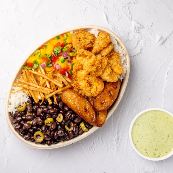 Overhead view of a Latin-inspired platter with fried chicken, rice, black beans, fries, plantains, mango salsa, and green sauce.